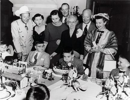 March 1956 - Roy Rogers, Mamie Eisenhower, Barbara Eisenhower, John Eisenhower, Elivera Doud, Dwight D. Eisenhower, and Dale Evans standing behind David Eisenhower at David's birthday party.