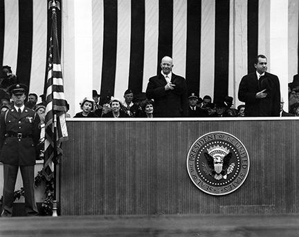 January 21, 1957 - Dwight D. Eisenhower and Richard Nixon place their hats over their hearts as the American flag passes the inaugural parade reviewing stand