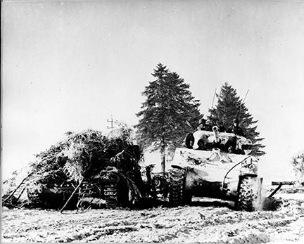Ardennes-Battle of the Bulge. January 15, 1945 - The first tank of a tank battalion passes a knocked out German tank on the road from Bertogne to Houffalize, Belgium.