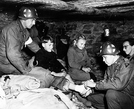 Ardennes-Battle of the Bulge. January 11, 1945 - Captain Charles S. Quinn (right) of Louisville, Kentucky, bandages gangrene infected foot of Belgian refugee child in cellar of house in Ottre, Belgium. Captain Quinn is a battalion surgeon with the 83rd Division, First Army.