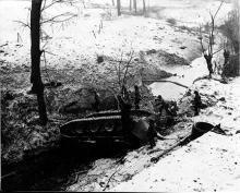 Ardennes-Battle of the Bulge. January 26, 1945 - Overturned German tank provides a bridge for 102nd Infantry Division troops crossing a small stream near Brachelen, Germany. Snow is on the ground.