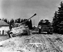 Ardennes-Battle of the Bulge. January 13, 1945 - Tank of 703rd Tank Battalion, 3rd Armored Division, moves past disabled German tank south of Langlir, Belgium.