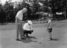 August 1, 1954 - Dwight D. Eisenhower, John Eisenhower, and David Eisenhower putt on green on the lawn of the main lodge while vacationing at Camp David